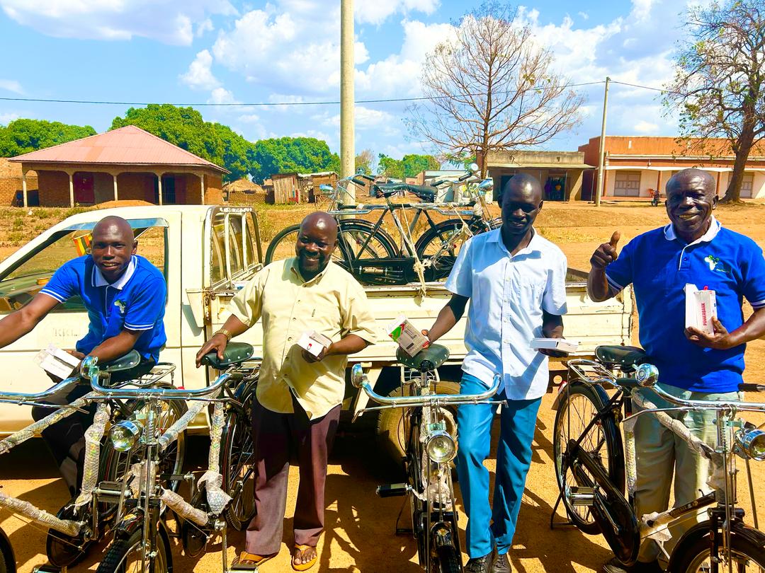 4 men stand in front of a trailer with unloaded bicycles. two are wearing bright blue uniform polo shirts. the others are wearing a yellow or blue shirt