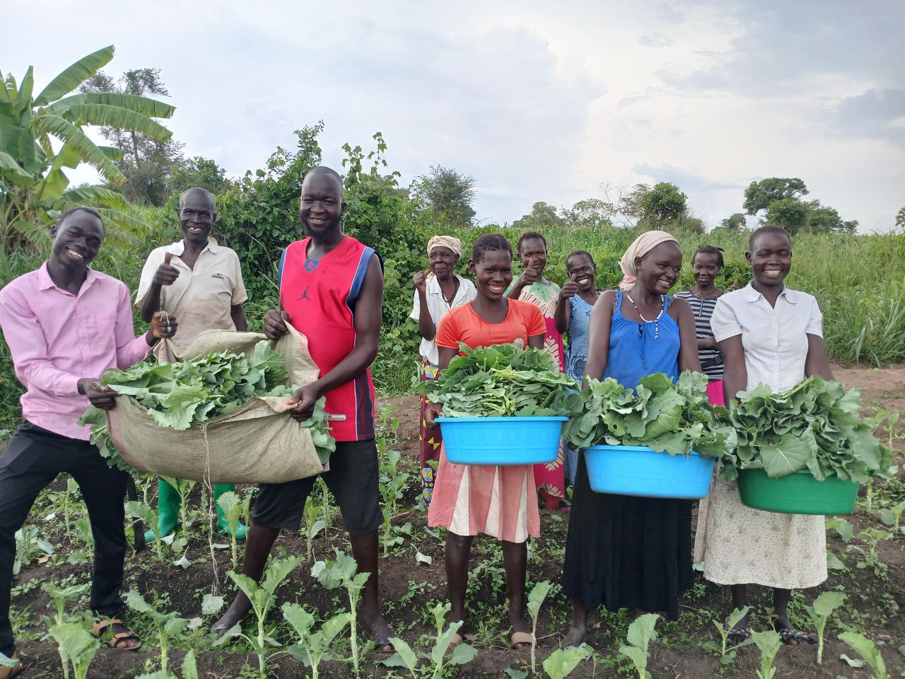Group is in a field facing camera. They are holding full baskets of green produce.