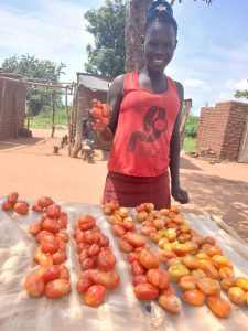woman in red top standing behind table with red tomatoes to be sold