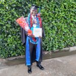 Man in cap and gown holding flowers and certificate, smiling