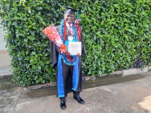 Man in cap and gown holding flowers and certificate, smiling