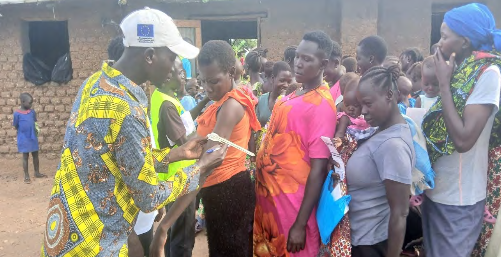 Group of women in bright colour clothes waiting to speak to doctor in white baseball cap and yellow patterned shirt