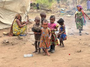 group of children facing camera, smiling. Wearing patterned dresses.