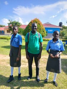 man in green top smiling. standing between two students in blue polo tops and long grey skirts
