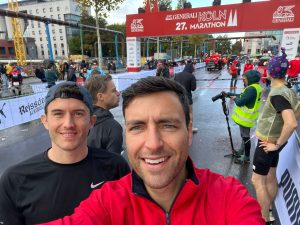 two men smiling. under red marathon banner.