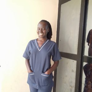woman in dark blue scrubs standing next to a white wall, smiling