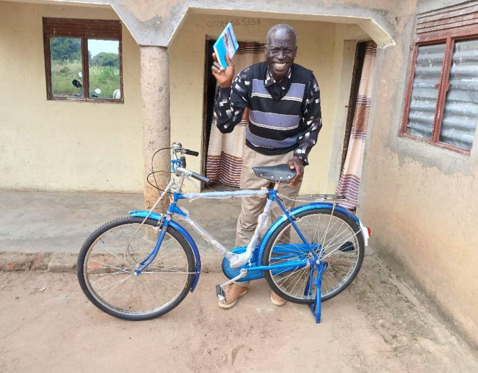 Man stands holding blue book and a blue bike. he is smiling very wide