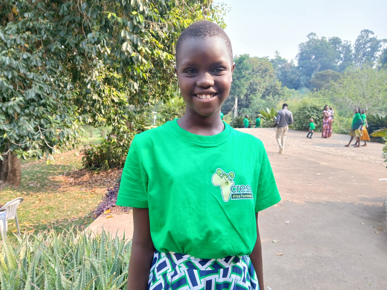 Girl in bright green tshirt, with yellow Africa logo and green patterned skirt.