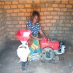 woman in blue polka dot dress couches behind a red generator and grinding machine.