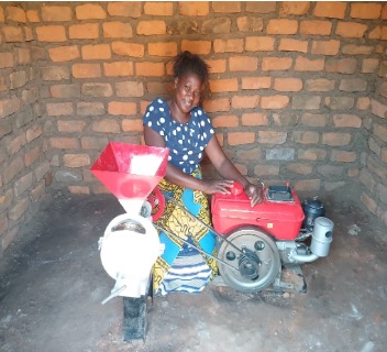 woman in blue polka dot dress couches behind a red generator and grinding machine.
