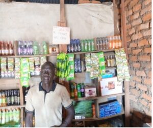 man in white polo stands in front of shelving. There are bottles and plastic packets in neon green, oragne and blue.