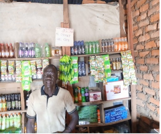 man in white polo stands in front of shelving. There are bottles and plastic packets in neon green, oragne and blue.