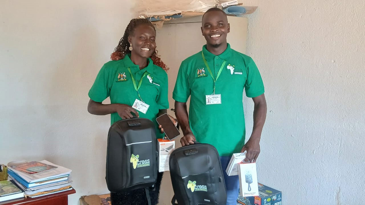 woman and man in green CRESS shirts smiling at camera. They are holding equipment for their jobs: backpack, phone,