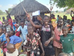 Group of children waving and smiling at camera, one of them is holding a football