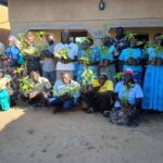 two lines of people - one standing, one crouching in front - holding up seedlings and smiling