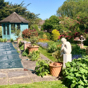 picture of a established garden. with sculpture of a woman, a covered pool, and a teal garden house at the end of the pool