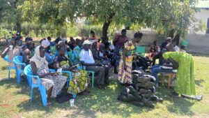 group sat on chairs arranged under a tree waiting to be given new agricultural equipment, including gum boots