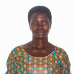 woman in front of white background. she has a small smile on her face. she is wearing an orange and green patterned dress