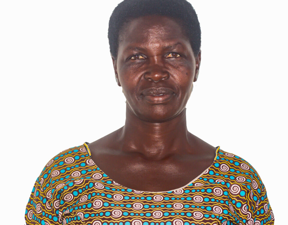 woman in front of white background. she has a small smile on her face. she is wearing an orange and green patterned dress
