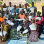 group of women kneeling and standing, posing for a picture. They are all holding small white bundles and smiling.