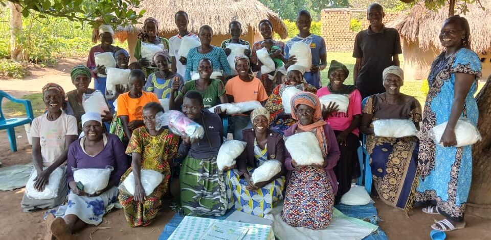 group of women kneeling and standing, posing for a picture. They are all holding small white bundles and smiling.